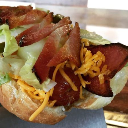 Bacon Cheeseburger Dog All-natural dog on a bun with cheddar cheese, thick sliced bacon, crumbled bacon, pickle spear, and shredded lettuce